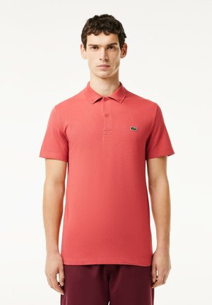 Polo rojo hecho de algodón con mangas cortas, que cuenta con un cuello clásico, una abertura de tres botones y un pequeño logo de cocodrilo verde en el pecho.