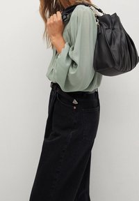 Zielona bluzka z długim rękawem i marszczonymi ramionami, zestawiona z czarnymi jeansami na wysokim stanie. Na ramieniu znajduje się czarna skórzana torba o teksturowanym wykończeniu.