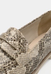 Μπεζ και κρεμ γόβες με σχέδιο φιδιού, που διαθέτουν υφαντή υφή, επίπεδη σόλα και διακοσμητική λεπτομέρεια με φιόγκο μπροστά.