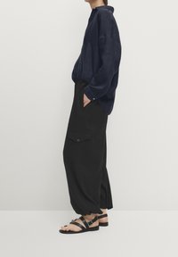 Laivastonsininen, pitkähihainen paita, jossa on kaulus; löysät mustat housut sivutaskuilla; mustat remmillä varustetut sandaalit; sileä kangaspinta.