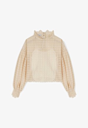 Blouse beige en dentelle à manches longues avec col montant à volants, poignets froncés, motif ajouré floral complexe et ourlet raccourci.