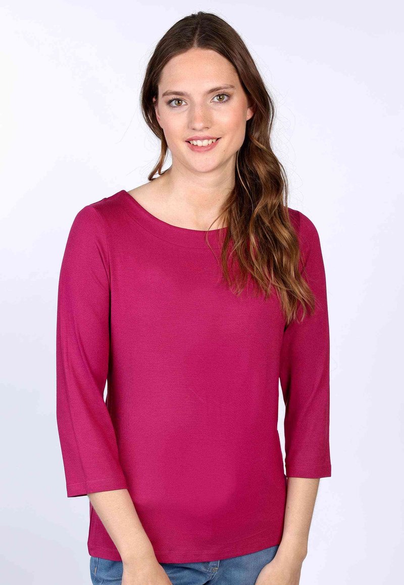 Magenta 3/4-Ärmel Oberteil mit rundem Kragen, glatter Textur und entspannter Passform, kombiniert mit hellblauen Jeans.