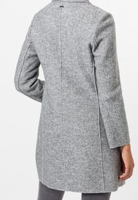 Szary, wełniany płaszcz o długości do kolan, z dopasowanym krojem, bocznymi rozcięciami i wyraźnymi przeszyciami. Posiada prosty kołnierz i fakturowane wykończenie.