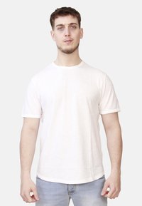 T-shirt grigio chiaro a maniche corte realizzata in tessuto morbido, con scollo rotondo e un'orlo posteriore leggermente più lungo, indossata con jeans blu.