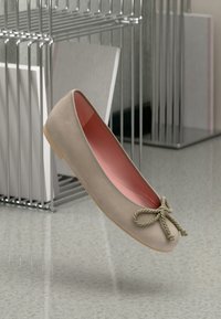 Beige balletlägenheter i mjukt mocka, med en rosa insida och en dekorerande grön repknut vid tån. Platt sula och rundad form.