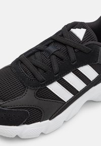 Zapatilla deportiva negra con materiales de malla y sintéticos, que presenta una parte superior texturizada, rayas blancas y una suela de goma blanca.