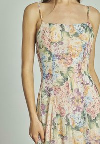 Robe florale avec décolleté carré, fines bretelles et jupe fluide. Fabriquée en tissu léger avec des motifs roses pâles, jaunes et violets.