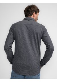 Button-up skjorte i marineblå med et subtilt hvidstribet mønster, der har lange ærmer og en buet søm. Tekstureret stof med klassisk krave.