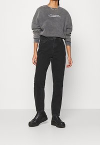 Felpa grigia con testo, vestibilità ampia, polsini a coste. Jeans neri a vita alta, gamba dritta, tessuto morbido. Scarpe platform nere con lacci.
