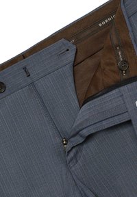 Niebieskie spodnie w prążki o gładkiej teksturze, z zapięciem na dwa guziki, zamkiem błyskawicznym oraz brązowym podszyciem. Dodatki obejmują czarne okucia.