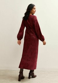 Bordowa sukienka w kwiaty z długimi bufiastymi rękawami, wcięciem w talii i długością sięgającą do połowy łydki, uzupełniona brązowymi botkami na obcasie.