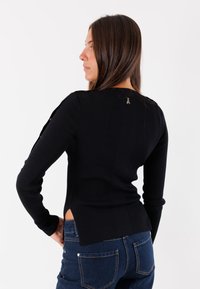 Maglione a coste nero con maniche lunghe, aperture laterali e un piccolo logo sulla parte posteriore. Abbinabile a jeans blu scuro.