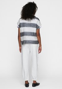 Top in lana a righe grigie e bianche con maniche corte, abbinato a pantaloni jogger grigi chiari e scarpe slip-on nere.