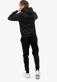 Completo felpa nera con felpa e pantaloni della tuta, realizzato in tessuto morbido. La felpa presenta un cordino e una tasca a marsupio; i pantaloni della tuta hanno una vita elastica.
