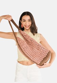 Háčkovaná taška s růžovým tělem a hnědým tkaným uchopem. Má otevřený síťový design a zaoblené dno, které ukazuje texturovaný povrch.