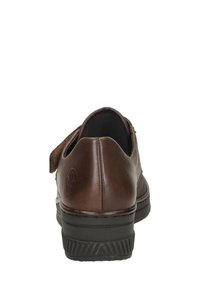 Zapato de cuero marrón con punta redondeada, parte trasera texturizada y suela de goma negra contrastante. Cuenta con una correa de velcro en el lateral.
