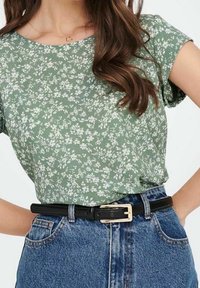 Top verde a maniche corte con stampa floreale realizzato in tessuto leggero, abbinato a una gonna di jeans a vita alta e una cintura nera con fibbia rettangolare.