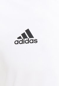 Camiseta blanca de tejido suave con un prominente logo negro de Adidas, que presenta tres rayas diagonales sobre el nombre de la marca.