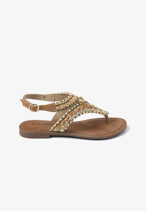 Beige platte sandaal met een teenpostontwerp, versierd met gouden en parelachtige kralen; heeft een bruine suede voetbed en een verstelbare enkelband.