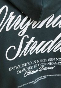 Sweatshirt à capuche vert foncé avec de grands graphismes en texte blanc. Texture douce avec un tissu côtelé et un design décontracté.