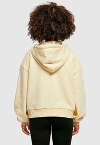 Sudadera con capucha color crema de corte relajado, con hombros caídos y puños acanalados. Tejido suave con una textura lisa y costuras mínimas.