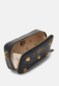 Černá prošívaná kosmetická taštička se zlatými prvky, včetně pyramidových akcentů a béžového interiéru s opakujícím se vzorem loga.