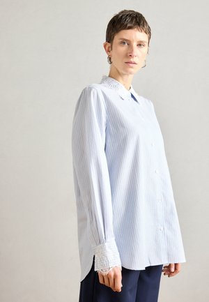 Világoskék csíkos ing, csipkés gallérral és mandzsettával, hosszú ujjakkal és gombos elülső záródással. Puha, texturált anyag.