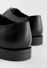 Schwarze Lederschuhe mit einer glatten Oberfläche, runder Zehenform und einer strukturierten Gummisohle. Nähte entlang der Ferse.