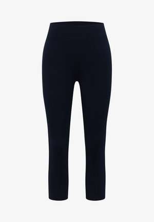 Gros plan d'une personne portant des leggings bleu marine et un haut à manches longues rose clair, le bras gauche reposant le long du corps.