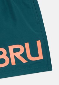 Calções desportivos em azul-petróleo feitos de tecido suave, com um logo laranja "BRU" na parte inferior direita. Costura visível ao longo das laterais.