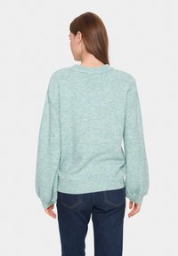 Ljus teal stickad tröja med avslappnad passform, ribbade ärmslut och nederkant, med en lätt svävande textur och mjukt tyg. Bärs med mörka jeans.