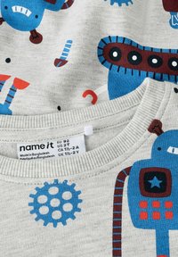 Camisa de algodón gris claro con gráficos de robots en azul y rojo, cuello redondo acanalado y una etiqueta de cuidado en el interior.