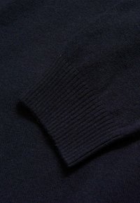 Dunkelblauer Strickpullover mit einem gerippten Bündchen und glatter Textur, der feine Garne mit subtilen Farbnuancen zeigt.