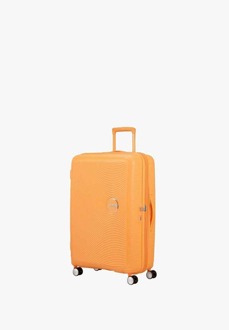 Valise rigide orange vif avec quatre roues pivotantes et une poignée rétractable, debout en position verticale sur un fond blanc.