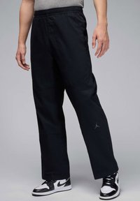 Black jogger pants with an elastic waistband, relaxed fit, and subtle texture. Features a small gray logo on the left thigh.