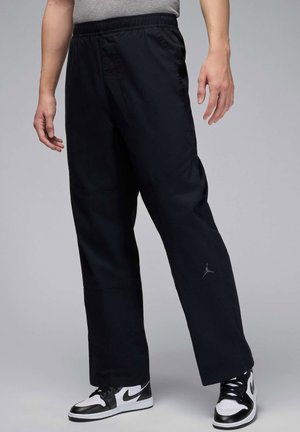 Black jogger pants with an elastic waistband, relaxed fit, and subtle texture. Features a small gray logo on the left thigh.