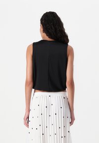 Svart ermeløs crop top med avslappet passform, med en subtil sømdetalj bak, kombinert med et flytende hvitt skjørt med svarte prikker.