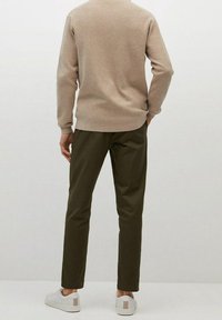 Pull en tricot marron clair associé à un pantalon vert olive. Modèle portant des baskets blanches avec des accents beiges, vu de dos.