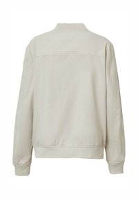 Giacca in cotone beige chiaro, stile bomber, con colletto e polsini a costine, texture liscia e dettagli delle cuciture sul retro.