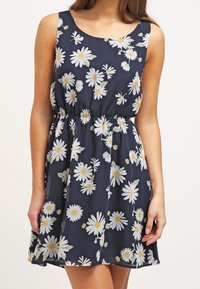 Námořnické modré šaty vyrobené z lehké tkaniny, s elastickým pasem a květinovým vzorem bílých sedmikrásek se žlutými středy.