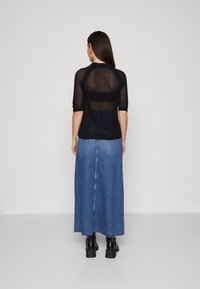 Črn mrežast top s kratkimi rokavi in polprosojno hrbtno stranjo, v kombinaciji z svetlo modro denim maxi krilo in črnimi debelimi čevlji.