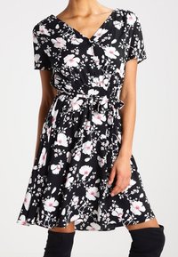 Abito floreale nero con maniche corte, caratterizzato da un design avvolgente, vita elastica e motivi floreali bianchi e rosa. Tessuto morbido e leggero.