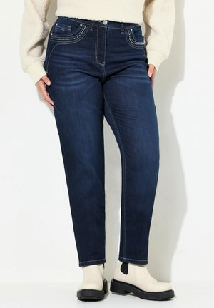 Tummansiniset farkut korkealla vyötäröllä, huomaamaton koristelu taskuissa ja suorat lahkeet. Yhdistetty vaaleansävyisiin nilkkureihin.