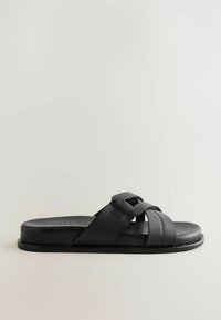 Schwarze Leder-Sandalen mit geschwungenen Riemen und flacher Sohle. Glatte Textur mit leichtem Glanz. Minimalistisches Design.