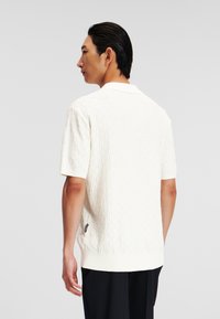 Korte mouwen, wit polo-shirt met een geprofileerd, geweven patroon. Voorzien van een kraag en een geribde zoom, zichtbaar label aan de linkerkant.