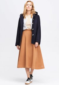 Mörkblå kappa med guldknappar, vit randig topp och en beige midikjol. Svarta snörskor med en vit och tan sula.