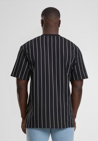 Tricou negru cu dungi verticale albe, mâneci scurte, guler rotund și o croială relaxată. Materialul pare neted, cu o textură minimă.