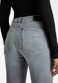 Jeans de mezclilla gris con un diseño ajustado, que cuentan con dos bolsillos traseros, detalles de costura sutiles y una cinturilla de cuero negro con marca.