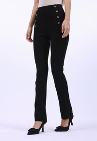Pantaloni neri a vita alta con dettagli in bottone dorato sui lati. Il tessuto è liscio, con un design slim fit e una leggera svasatura all'orlo.