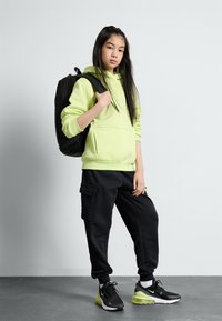 Felpa con cappuccio verde neon e pantaloni jogger cargo neri, abbinati a sneakers nere e lime. Progettata con tasche e uno zaino nero.
